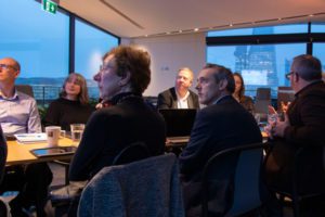 Boardroom meeting, staff sat around table discussing plans.